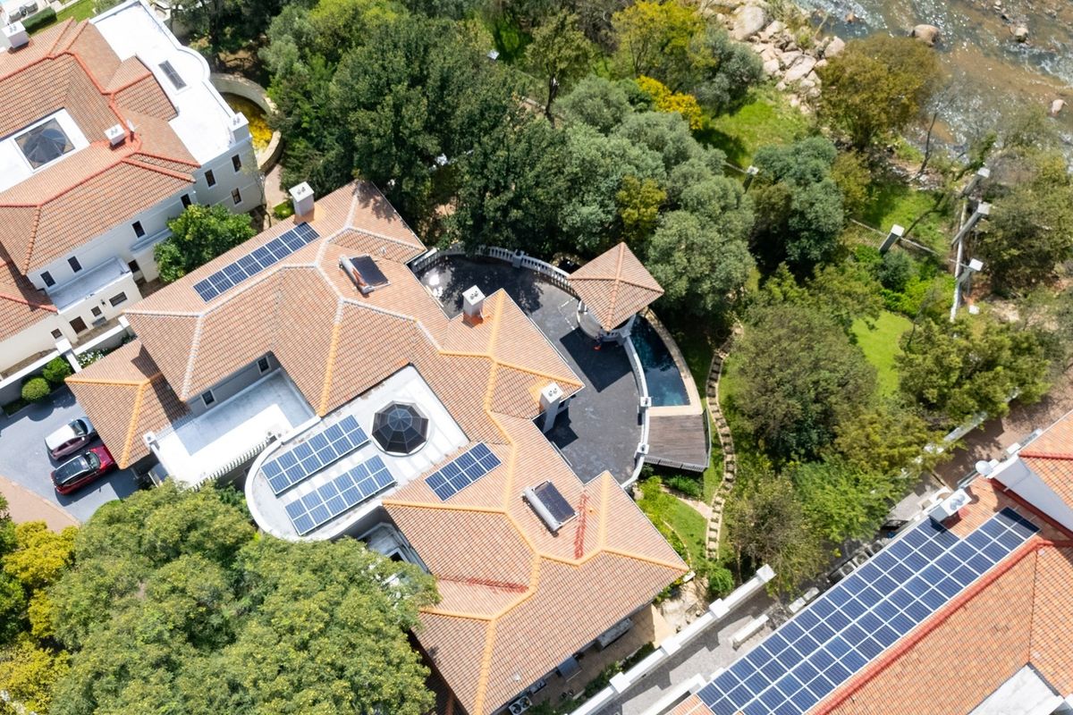 Aerial view of a residential property featuring a tiled roof with integrated solar panels, a swimming pool, and landscaped garden surroundings.