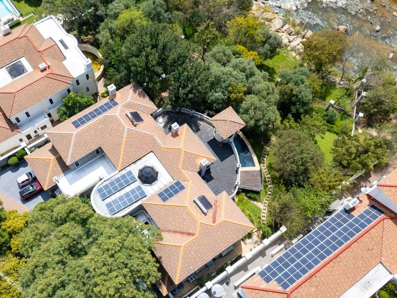 Aerial view of a residential property featuring a tiled roof with integrated solar panels, a swimming pool, and landscaped garden surroundings.