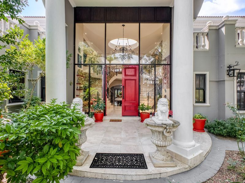 Grand entrance featuring a striking red door, double-height glass facade, classical columns, and a stone-tiled porch with elegant architectural detailing.