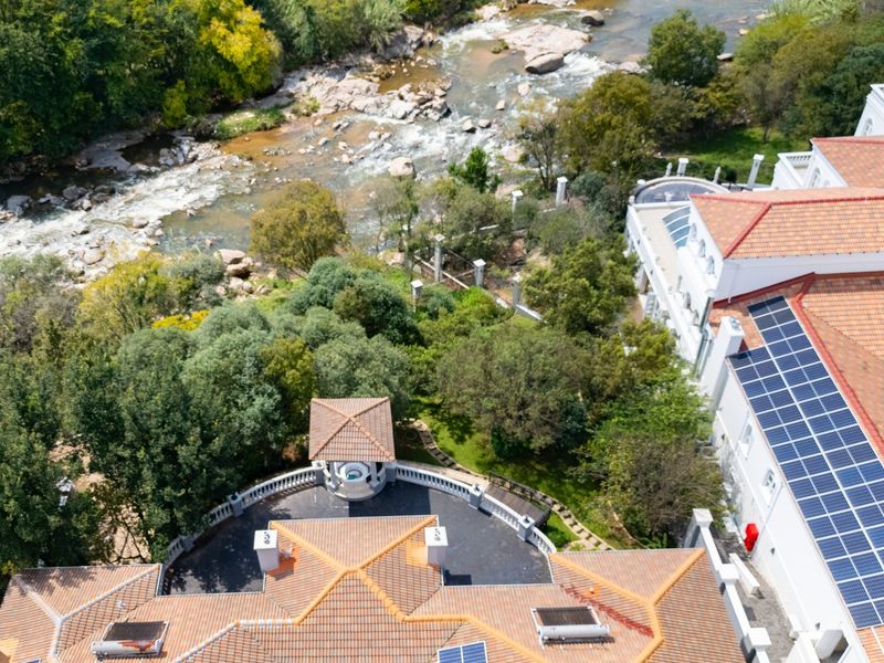 Aerial view of a large property featuring extensive solar panel installations, terracotta roofing, and a scenic garden overlooking a river.