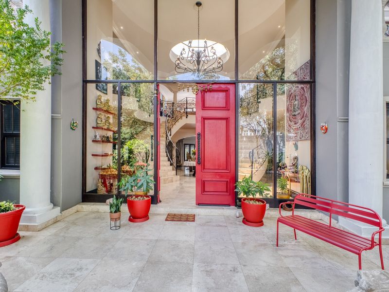 Grand entrance featuring a striking red door, double-height glass facade, and an elegant wrought iron staircase visible through the entryway.