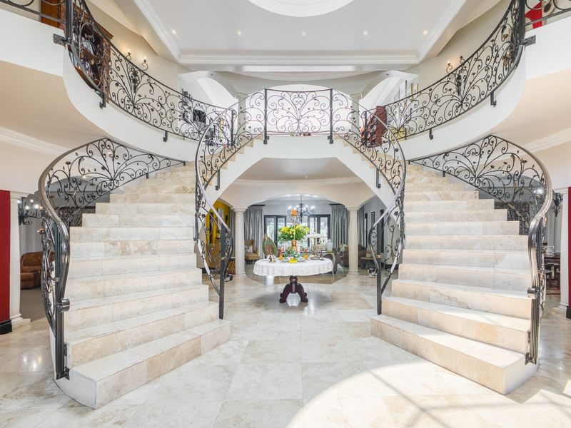 Grand entrance hall featuring a symmetrical dual staircase with ornate wrought iron balustrades and polished stone flooring.