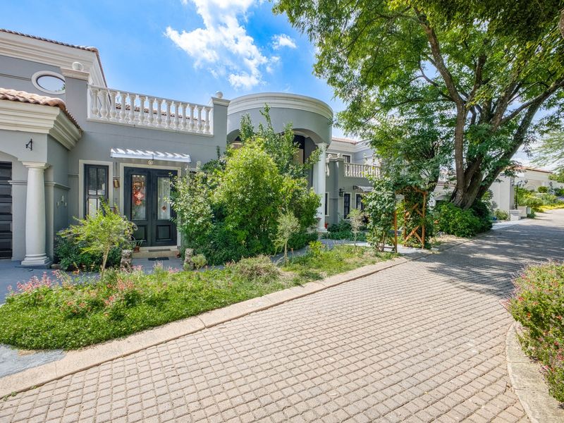 A well-maintained front elevation featuring a paved driveway, classic architectural columns, a decorative balustrade, and established garden landscaping.