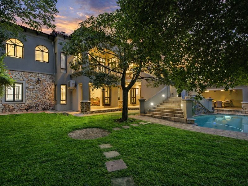 A beautifully landscaped rear garden featuring a swimming pool, stone-clad facade, covered patio, and an elegant outdoor staircase leading to the upper level.