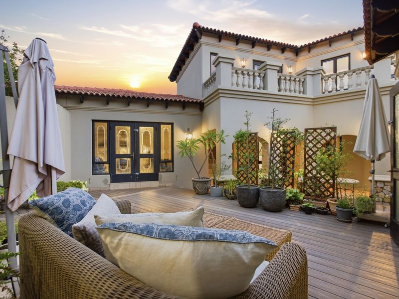 A well-maintained rear courtyard featuring timber decking, a balcony with balustrade, and elegant double glass doors at sunset.