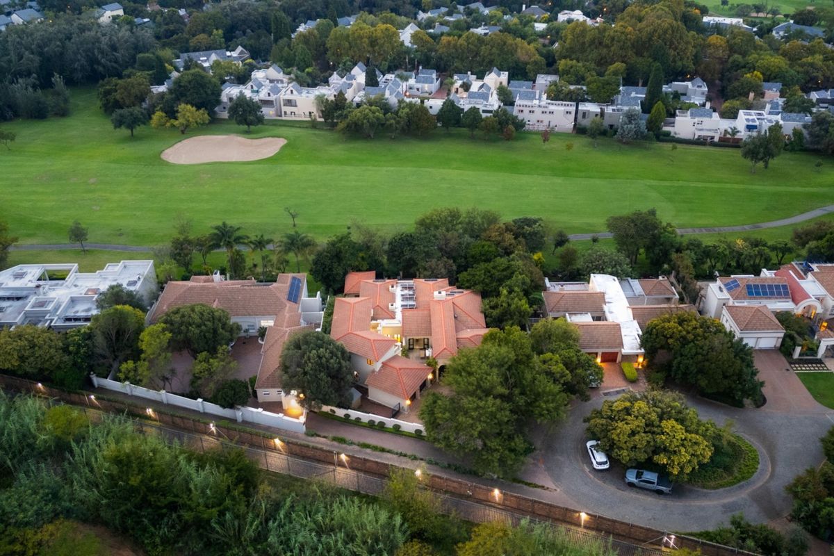 Aerial view of a residential property featuring a tiled roof, solar panels, and a paved driveway, situated adjacent to a golf course.