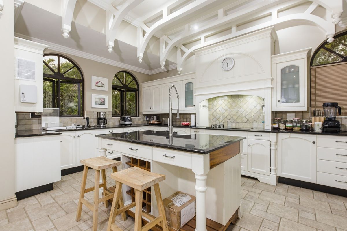 Spacious kitchen featuring a central island, granite countertops, custom cabinetry, decorative ceiling trusses, and large arched windows providing natural light.