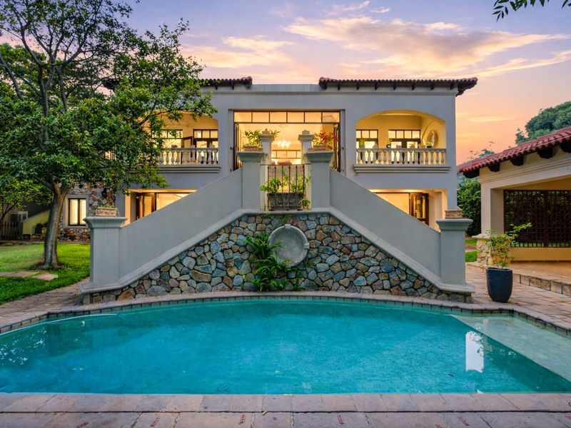 Rear elevation featuring a swimming pool, stone-clad feature wall, central staircase, and upper-level balcony with classic architectural detailing.