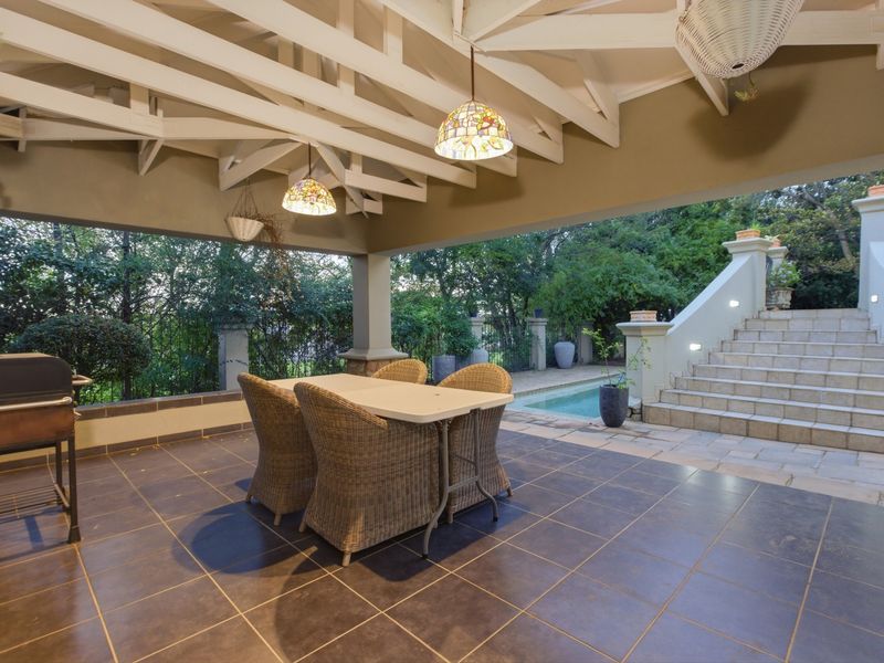 A spacious covered patio featuring exposed timber rafters, tiled flooring, and direct access to a swimming pool and stone staircase.