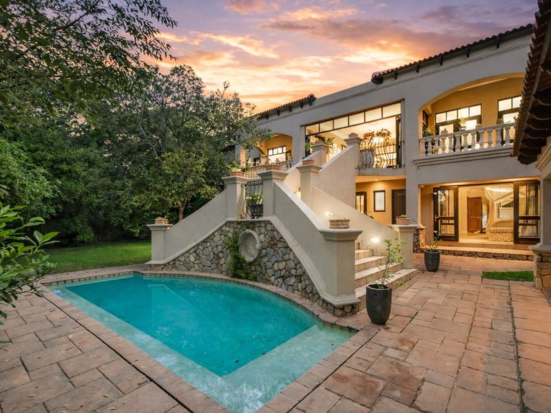 Rear exterior view featuring a swimming pool, stone-clad staircase, paved patio area, and a balcony overlooking the garden.