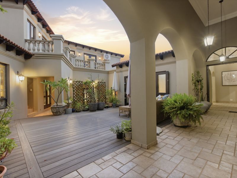 A spacious covered patio featuring elegant arched columns, a mix of composite decking and stone tile flooring, and access to the upper balcony level.