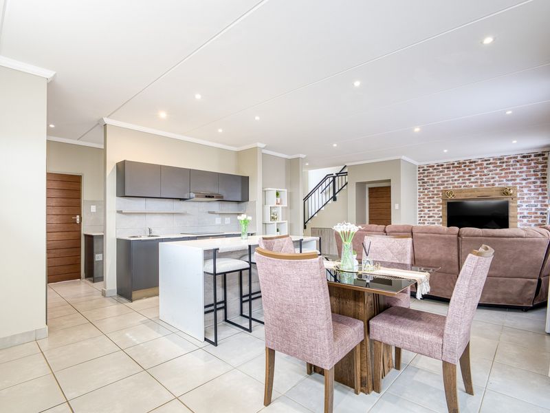 Modern open-plan living area featuring a sleek kitchen with island, dining space, and a striking exposed brick feature wall with staircase access.