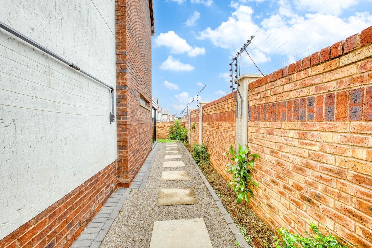 A side passage featuring a paved walkway, gravel landscaping, and a secure brick boundary wall with electric fencing.