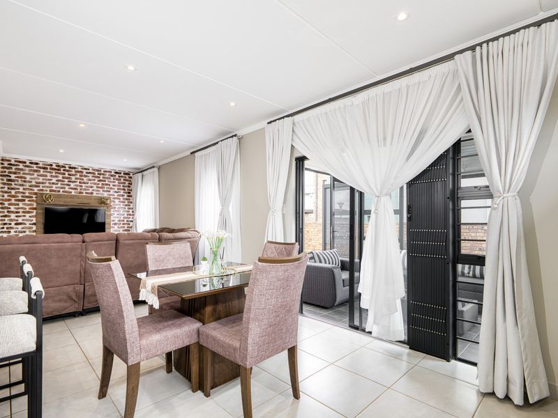 Spacious open-plan living and dining area featuring a striking exposed brick feature wall, tiled flooring, and large sliding doors leading to the patio.