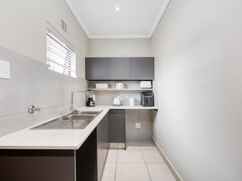 A modern, well-maintained scullery featuring sleek dark cabinetry, stone countertops, a double sink, and neutral tiled finishes.
