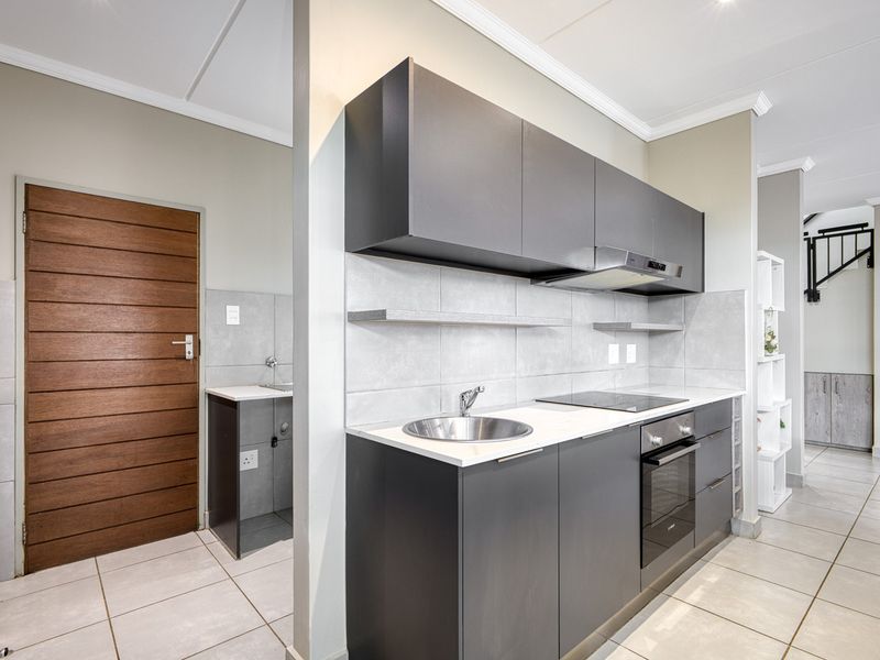 Modern kitchen featuring dark cabinetry, stone countertops, integrated electric hob, oven, extractor fan, and a secondary scullery area with a sink.