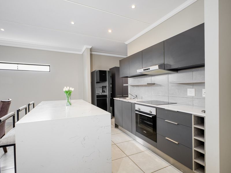 Modern kitchen featuring a large quartz island, sleek dark cabinetry, built-in oven, electric hob, and recessed lighting in a clean, contemporary space.