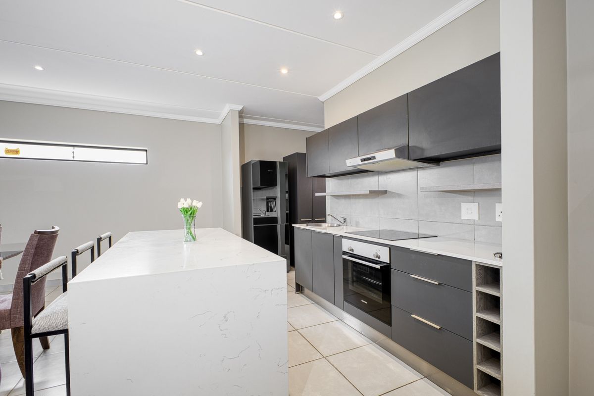 Modern kitchen featuring a large quartz island, sleek dark cabinetry, built-in oven, electric hob, and recessed lighting in a clean, contemporary space.