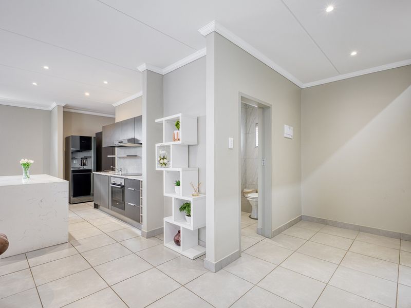 Modern open-plan living area featuring a sleek kitchen with stone island, built-in appliances, tiled flooring, and recessed lighting, leading to a separate bathroom.