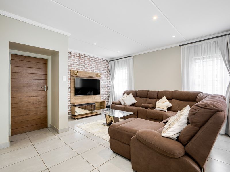 A well-maintained living room featuring an exposed brick accent wall, neutral tiled flooring, and modern recessed lighting.
