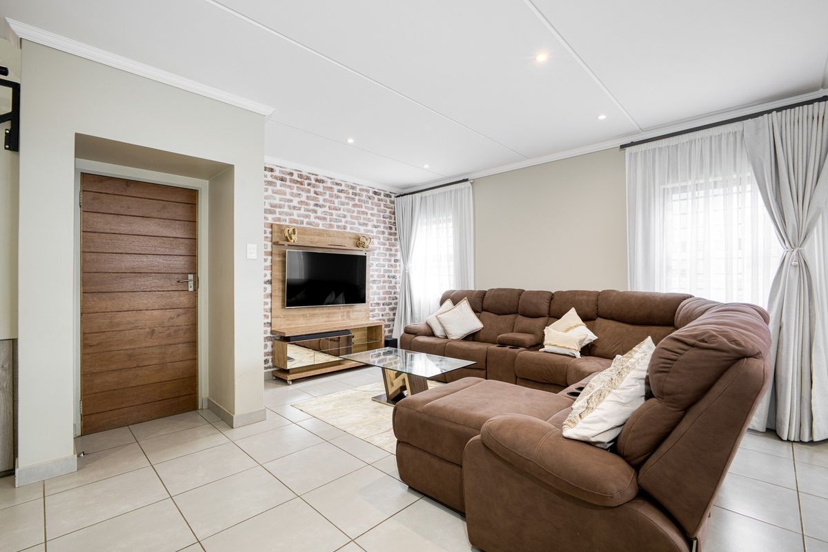 A well-maintained living room featuring an exposed brick accent wall, neutral tiled flooring, and modern recessed lighting.