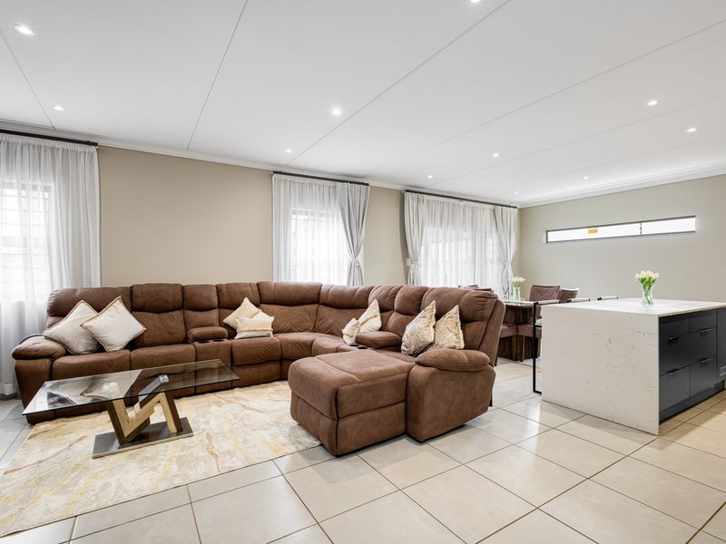 Spacious open-plan living and kitchen area featuring modern tiled flooring, recessed downlighting, and a sleek kitchen island with a stone countertop.
