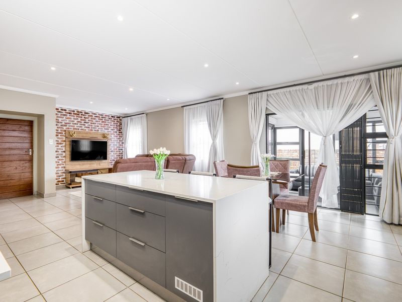 Spacious open-plan living area featuring a modern kitchen island with stone countertop, tiled flooring, and an exposed brick feature wall leading to a patio.