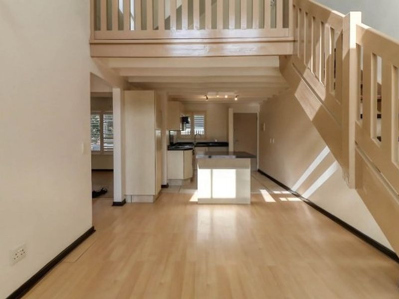 Open plan living area featuring a wooden staircase leading to a mezzanine level and a functional kitchen with island cabinetry.