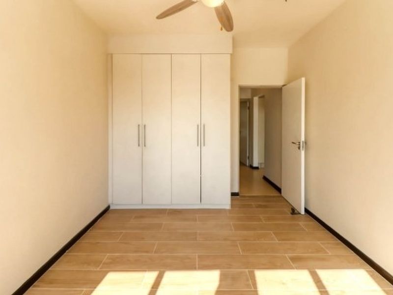 An empty bedroom featuring neutral tiled flooring, built-in cupboards, and a ceiling fan, offering a clean and versatile space.