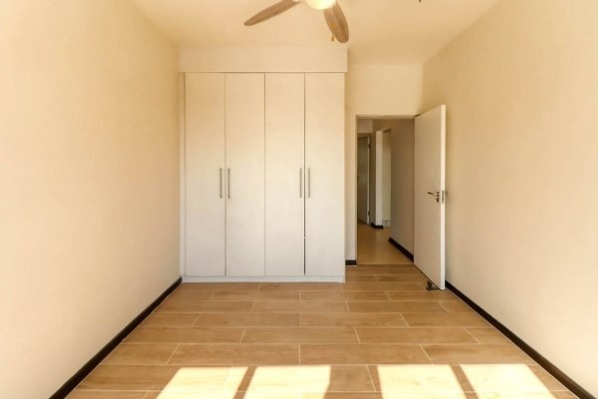 An empty bedroom featuring neutral tiled flooring, built-in cupboards, and a ceiling fan, offering a clean and versatile space.