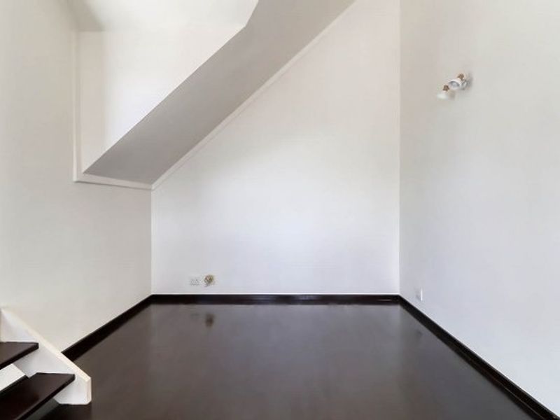 A bright, empty living area featuring dark wood flooring, a unique sloped ceiling, and clean white walls, ready for personalization.