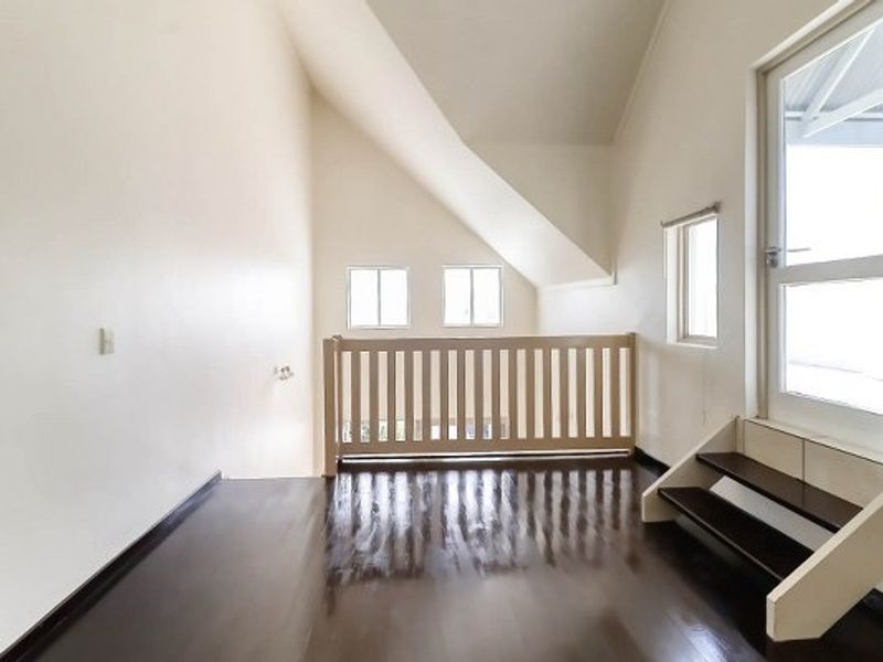 An empty, light-filled living area featuring polished timber flooring, a vaulted ceiling, and a staircase leading to an upper level with a safety railing.