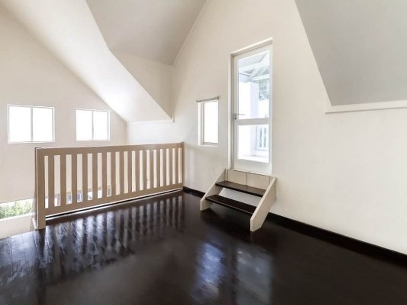 An empty, bright living area featuring vaulted ceilings, dark timber flooring, and a balustrade overlooking the lower level with direct access to an outdoor space.