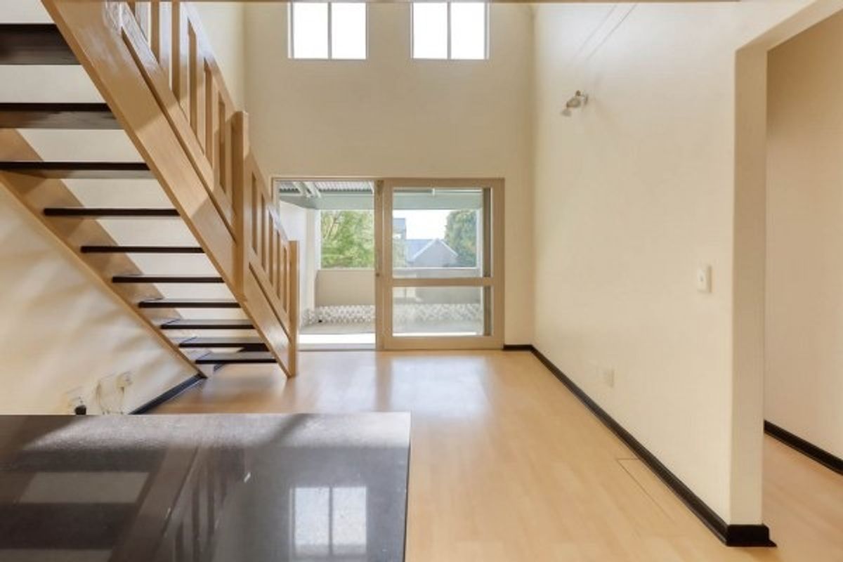 Spacious double-volume living area featuring light laminate flooring, a wooden staircase, and sliding glass doors leading to an outdoor balcony.