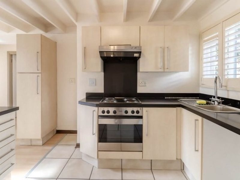 A clean, functional kitchen featuring light-toned cabinetry, stainless steel appliances, tiled flooring, and exposed ceiling beams, offering a bright and practical workspace.