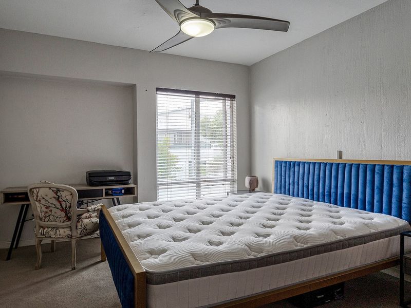A functional bedroom featuring carpeted flooring, a ceiling fan, and venetian blinds, providing a comfortable and well-lit space.