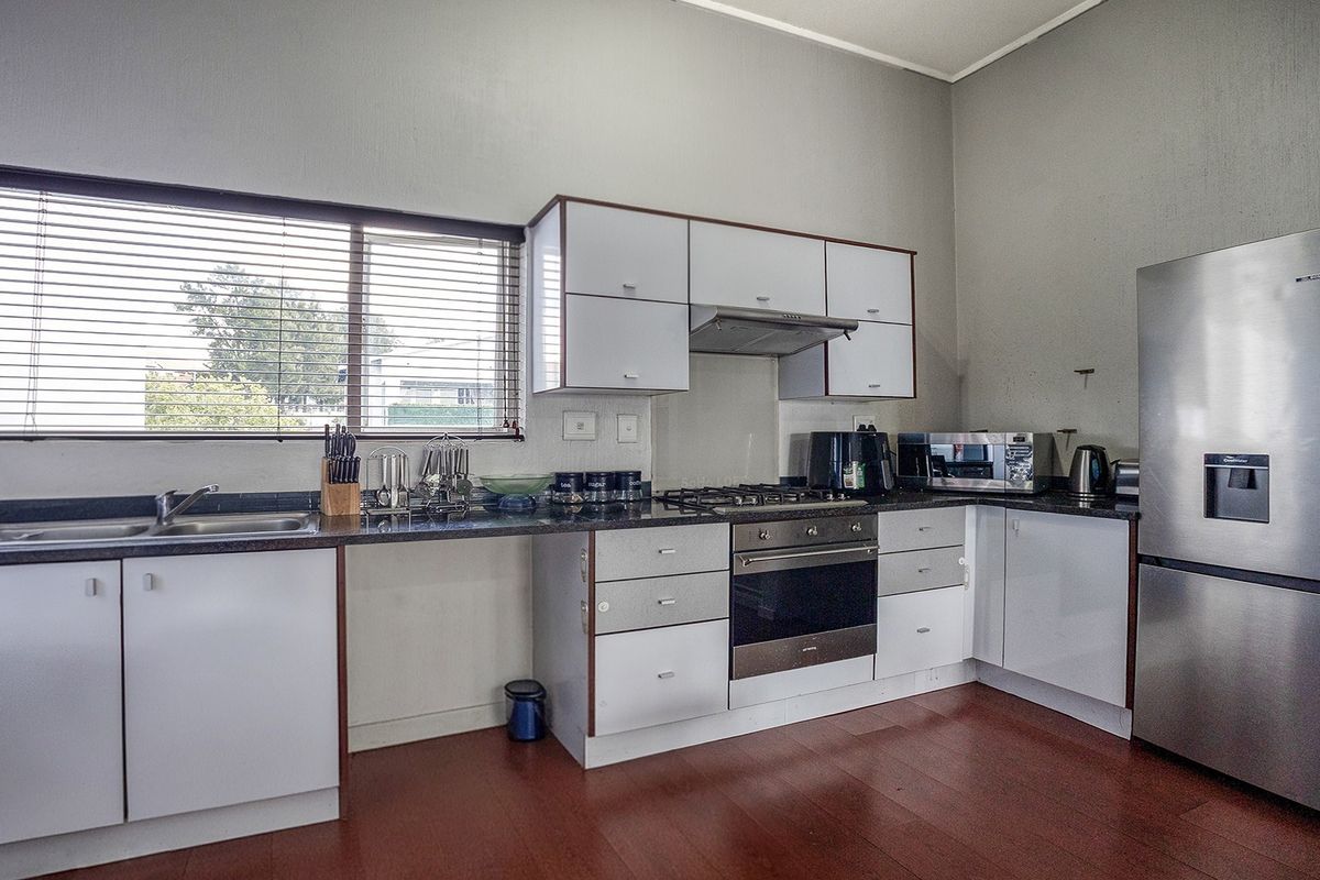 A functional kitchen featuring white cabinetry, dark laminate countertops, a gas hob with extractor fan, and integrated stainless steel oven.
