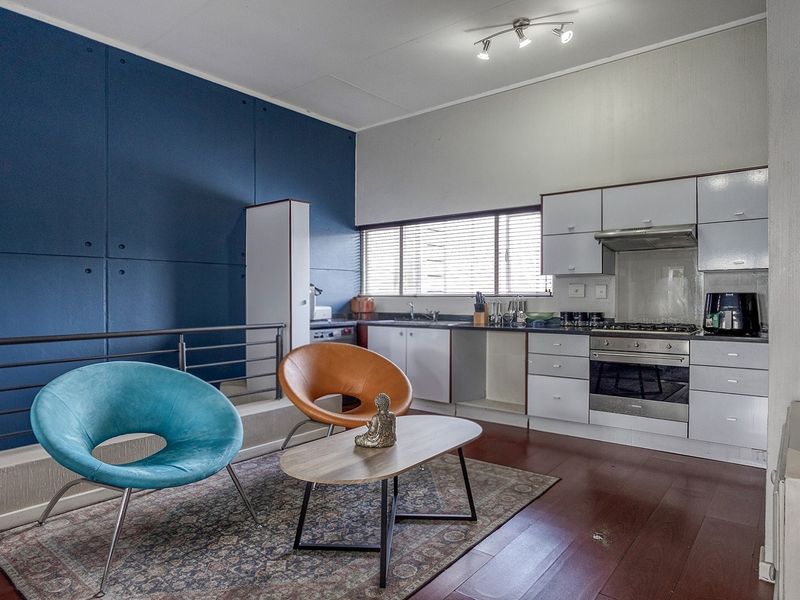 Open-plan living area featuring a compact kitchen with built-in cabinetry, stainless steel appliances, and laminate flooring, overlooking a lower level via a metal balustrade.