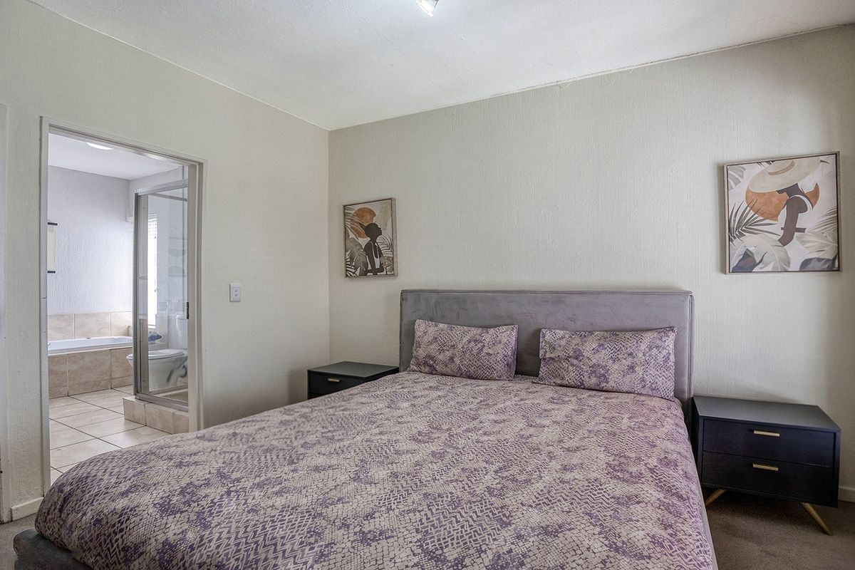 A bedroom featuring an en-suite bathroom with a glass shower enclosure and a built-in bathtub, finished with neutral wall tones.