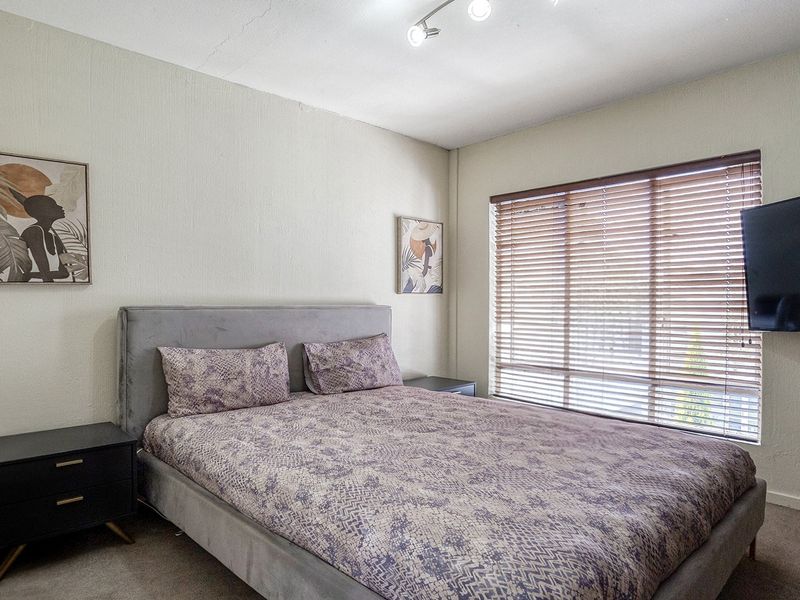 A bedroom featuring textured walls, track lighting, and venetian blinds over the window.