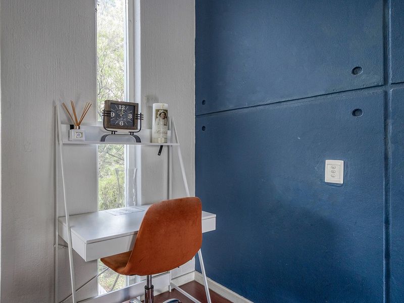 A compact office space featuring a tall vertical window and a bold blue textured feature wall.