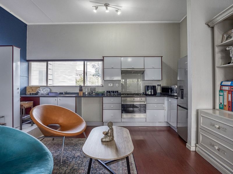Open plan kitchen and living area featuring laminate flooring, built-in cabinetry, and integrated stainless steel appliances.