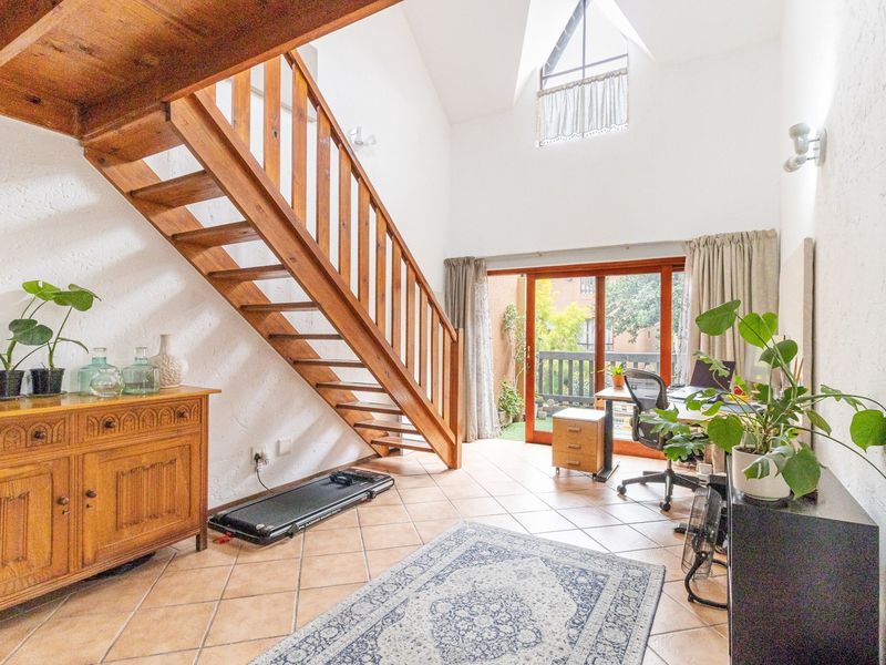 Spacious living area featuring a prominent wooden staircase, vaulted ceilings with high-level windows, and sliding glass doors leading to an outdoor balcony.