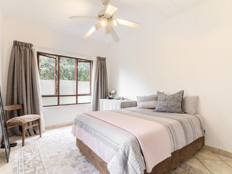 A well-lit bedroom featuring tiled flooring, a ceiling fan, and a window with natural light.