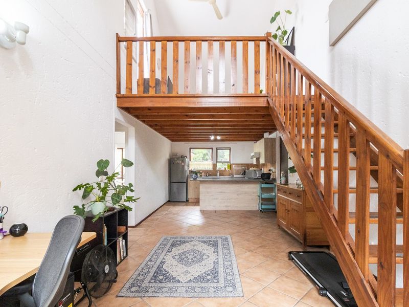 Open plan living area featuring a wooden staircase leading to a mezzanine level, tiled flooring, and a functional kitchen space.