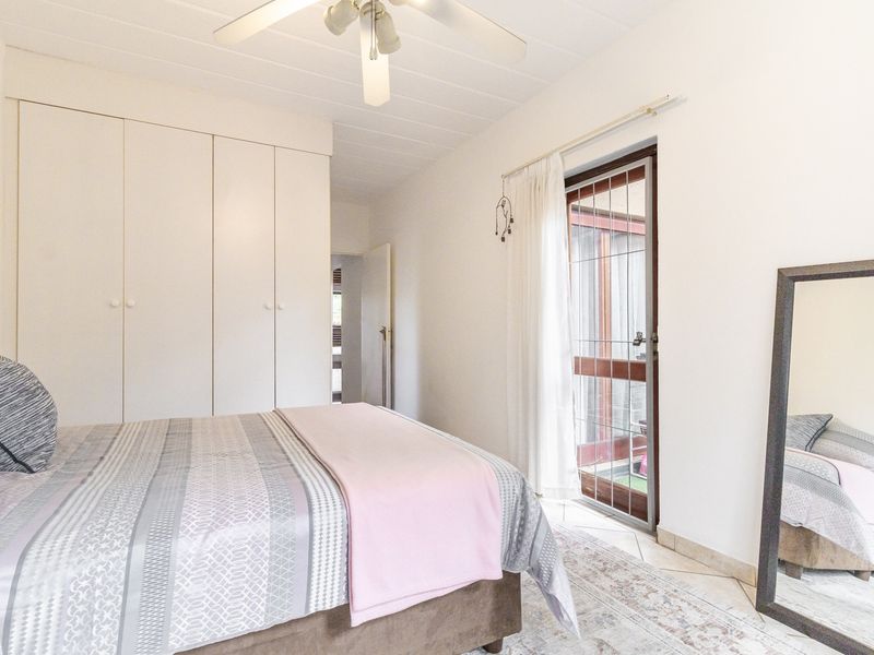 A bedroom featuring built-in cupboards, a ceiling fan, tiled flooring, and direct access to an outdoor area through a security gate.