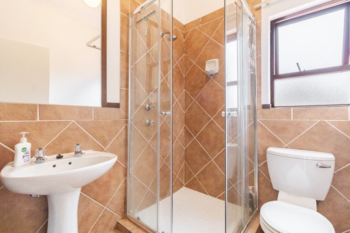 A functional bathroom featuring a pedestal basin, a glass-enclosed shower, and a toilet, finished with neutral-toned wall and floor tiles.