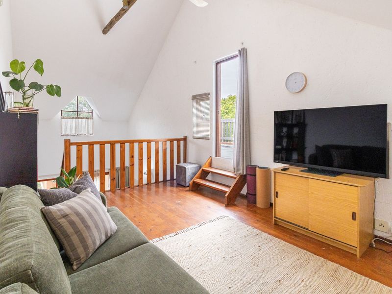 A cozy loft-style living room featuring vaulted ceilings, exposed timber beams, warm timber flooring, and a wooden balustrade overlooking the lower level.