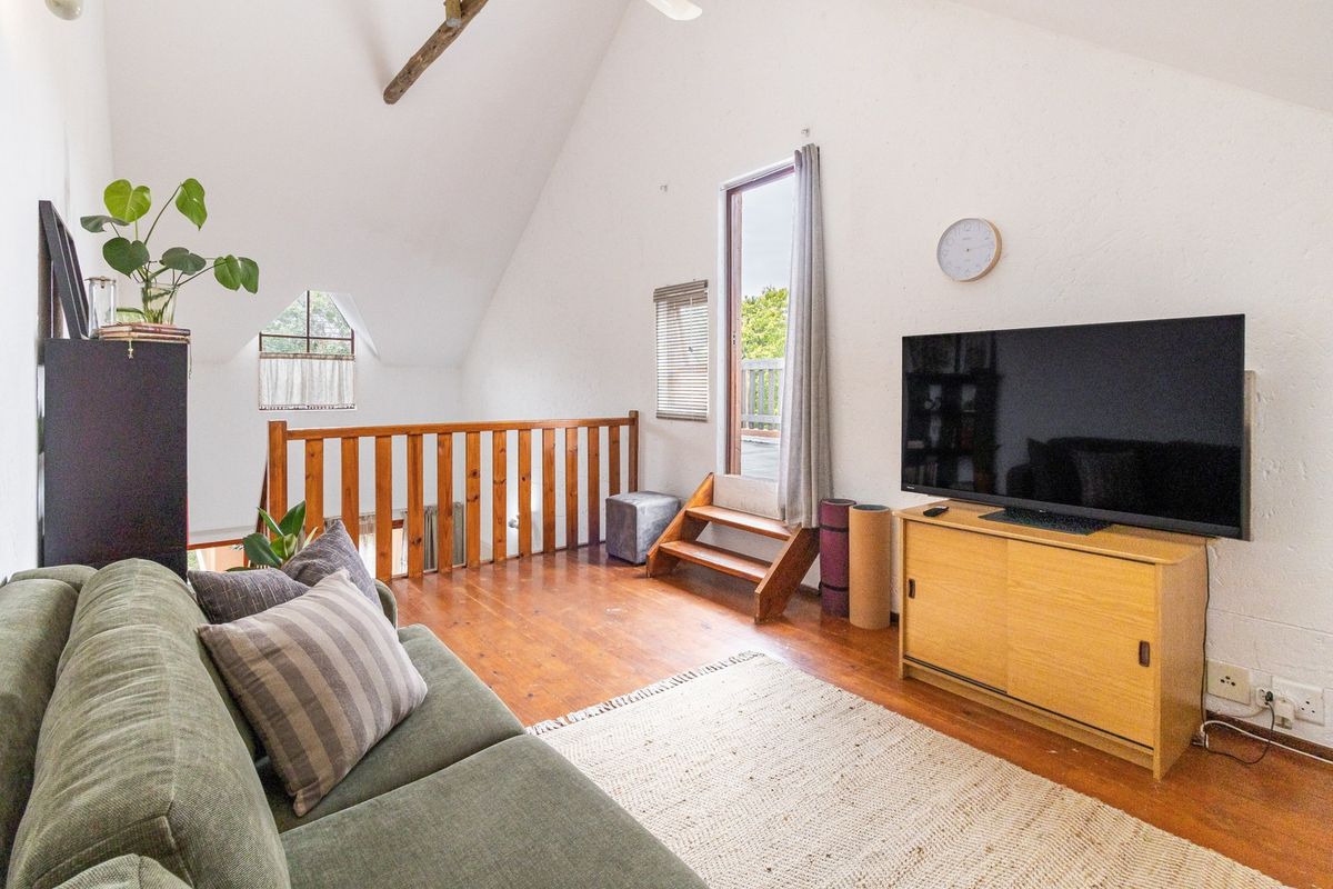 A cozy loft-style living room featuring vaulted ceilings, exposed timber beams, warm timber flooring, and a wooden balustrade overlooking the lower level.