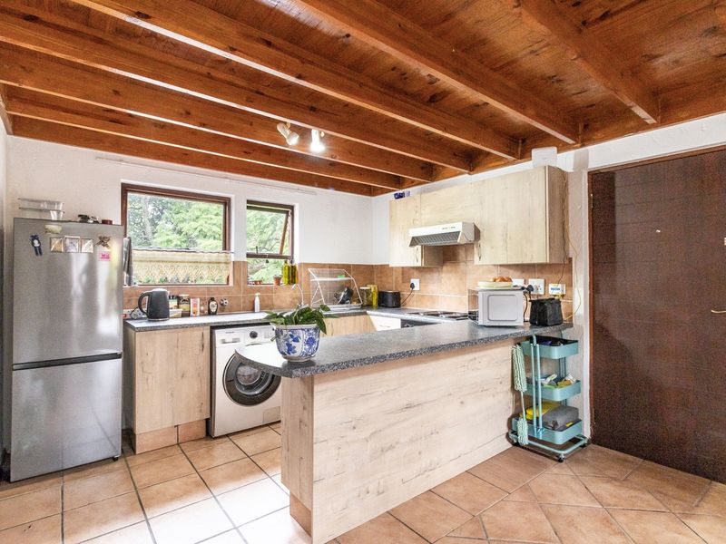 Functional kitchen featuring laminate cabinetry, granite countertops, tiled flooring, and an exposed timber beam ceiling, providing a practical workspace with integrated appliance connections.